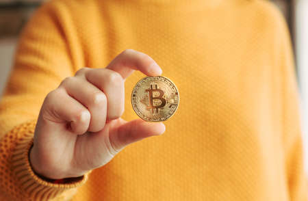 Woman showing a golden bitcoin in her hand. BTC and cryptocurrencies business in a digital...