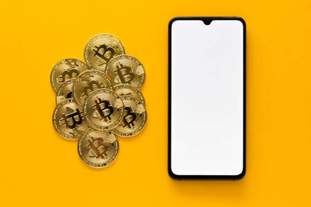 Overhead view of some of bitcoins and mobile phone mockup on a yellow background. Golden BTC coins, Stock Market of cryptocurrencies and decentralized finances conceptの写真素材