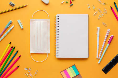Stock photo of back to school concept in the new normal with a mask, a blank notebook mockup and several stationery objects on a yellow backgroundの写真素材