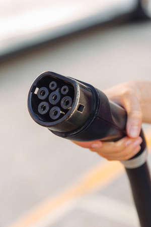 Close-up view of an electric car or EV plug held by a hand in a charging station. Electrical power supply in a power station and Eco-friendly alternative energy conceptの写真素材