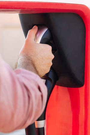 Man's hand holding an EV or electric car socket in a charging station. Electrical power supply in a power station and Eco-friendly alternative energy conceptの写真素材