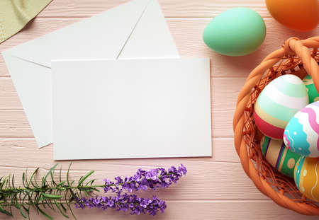 Happy Easter greeting card mockup, blank paper with pastel color eggs, basket, flowers and wooden...