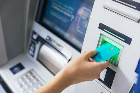 Close up of a girl inserting a credit card in ATM bank machine to transfer money or withdraw. Finance customer and banking service conceptの写真素材