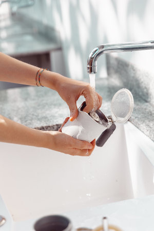 Hands of a woman cleaning the parts of a moka coffee maker under a stream of waterの写真素材