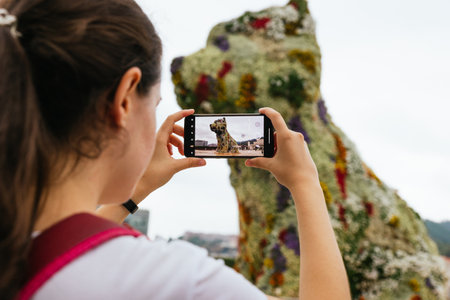 Bilbao, Spain - September, 2022: A young female tourist taking a photo of Puppy, the floral dog sculpture designed by Jeff Koons, in front of the Guggenheim museum of Bilbao, Spainのeditorial素材