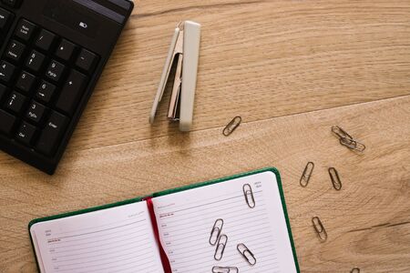 Keyboard, Stapler and paper clips with notebook on wooden table