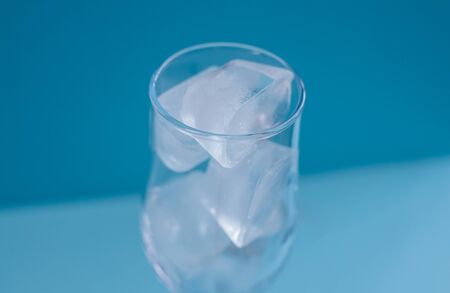 A glass of ice on a blue background. Tableware for alcohol. A glass for champagne and wine. Chilled...