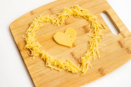 Cheese in the shape of a heart on a wooden Board. Grated cheese in the shape of a heart. Hard cheese.Cheese is for lovers.の写真素材