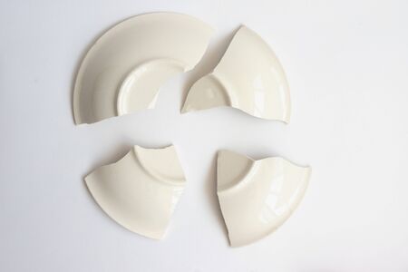 A broken white ceramic plate on the white floor. Fragments of a plate on a white background.Tableware.の写真素材