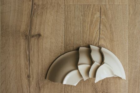 A broken white ceramic plate on the wooden floor. Broken dishes. Fragments of a plate.の写真素材