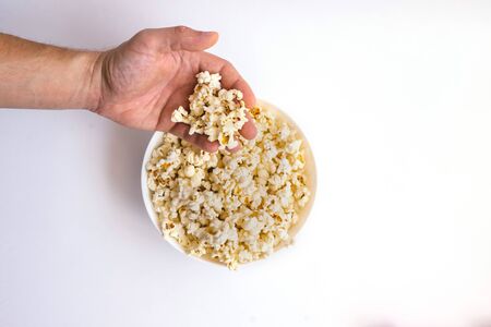 Hand takes popcorn from a white plate on a white background. Delicious snack. A lot of popcorn on a plate.の写真素材