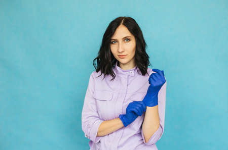 A young girl puts on blue medical gloves. A nurse or doctor is preparing for work. A girl in a...