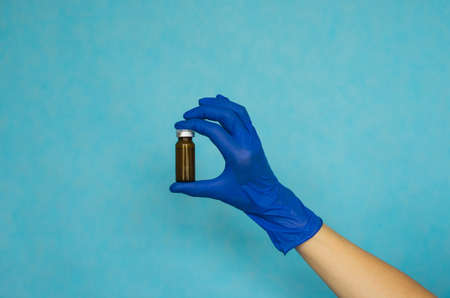 A woman's hand in blue gloves holds an ampoule. Vaccine. The ampoule with the medicine. Medication for injection.の写真素材
