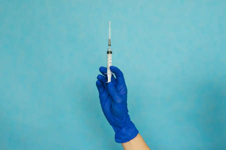 A woman's hand in blue medical gloves holds a syringe on a blue background. Medical procedure.の写真素材