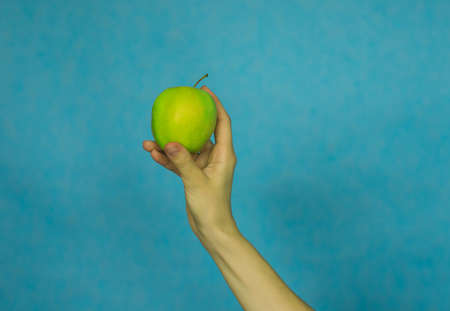 A woman's hand holds a ripe Apple on a blue background. Healthy diet.Vitamins.
