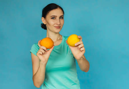 A young girl is holding an orange and a lemon. Tropical fruit. Girl on a blue background.の写真素材