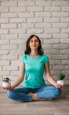 A young girl meditates in her home. The girl holds indoor plants in her hands. Flower pot in the hands of a girl.の写真素材