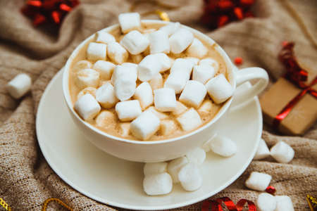 Coffee with marshmallows on a background of knitted fabric with gifts and holiday bows.Hot winter...