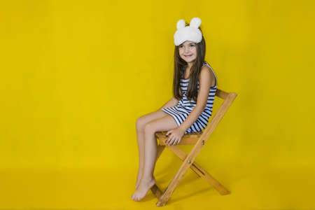 Little girl on a bright yellow background wearing a fashion accessory sleep mask, sitting on a...
