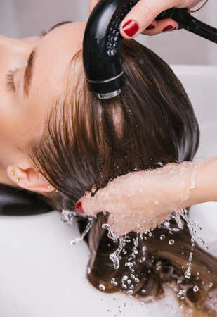 A young woman washes her hair with shampoo in a Barber shop. Professional hair care products. Beauty salon.の写真素材
