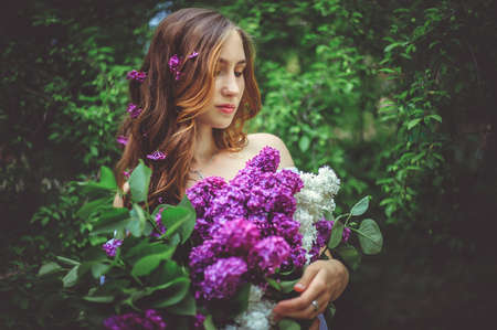 A young woman is holding a beautiful bouquet of lilacs.The girls hair is loose.Flowers in your hair.の写真素材