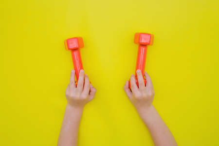 Childrens hands hold red dumbbells on a yellow background.の写真素材
