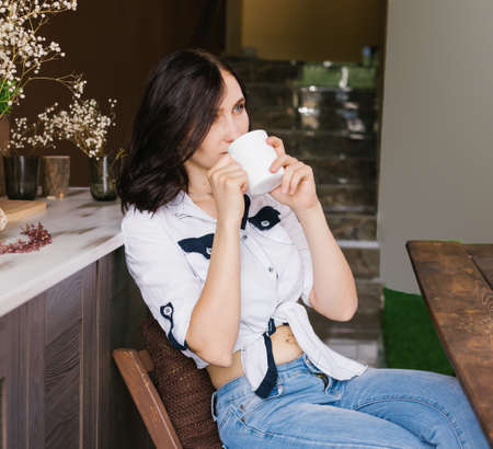 Beautiful sweet smiling young woman sitting at the table and drinking coffee or tea.