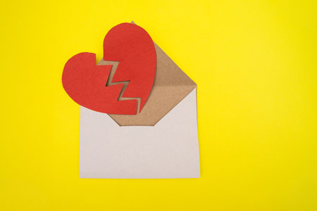 Paper heart cut in two halves in an envelope on a yellow background.The concept of separation and divorce. Heart made of red cardboard.の写真素材