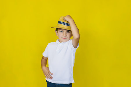 A little boy in a white shirt and straw hat on a yellow background. The gaze is directed at the camera.the concept of recreation and tourism.In the school holidays.の写真素材