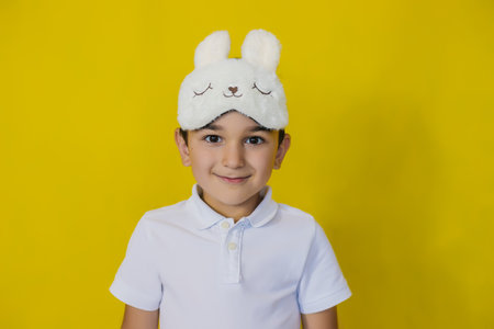 A little boy on a bright yellow background in a fashionable accessory sleep mask. The concept of a...