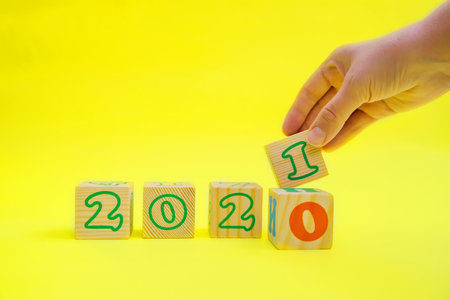 The female hand removes the wooden cube with the number 0 and places a new cube with the number 1 on a yellow background. The concept of a New year.の写真素材