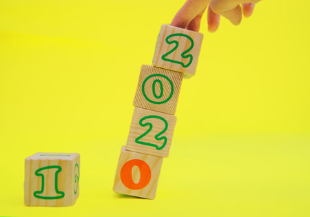 Wooden cubes with the numbers 2021 on a yellow background. The concept of a New year.New date The cubes are stacked on top of each other and a woman's hand pushes the tower. The cubes fall.の写真素材