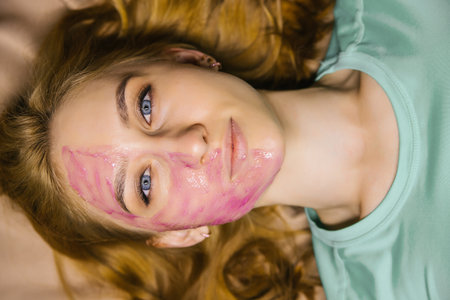 young woman with a pink cosmetic mask on her face. Facial skin care. The girl smiles and looks at the camera.の写真素材