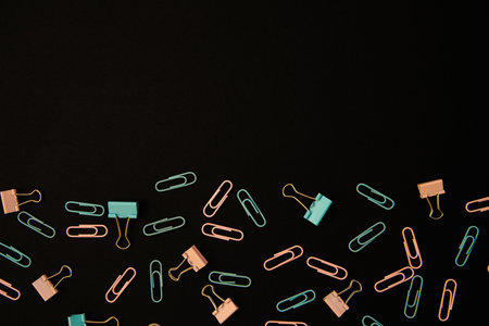 Paper clips and clips in blue and pink are scattered on a black background. Office supplies....