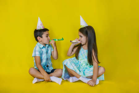 A little girl and a boy are sitting on the floor in their holiday hats. The children blow their...