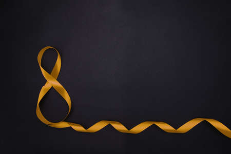 On a black background, a yellow satin ribbon in the form of an eight. Gift wrap.