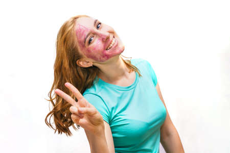 A young woman with a purple cosmetic mask. A woman shows a sign of Victoria. Facial skin care. A girl on a white background.の写真素材