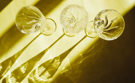 Empty glasses stand on a yellow background, top view. A beautiful creative still life filled with light with hard shadows and highlights from the glass. Sunlight is refracted through the glass.の写真素材