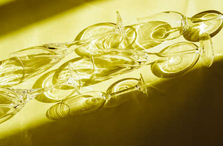 Empty glasses stand on a yellow background, top view. A beautiful creative still life filled with light with hard shadows and highlights from the glass. Sunlight is refracted through the glass.の写真素材