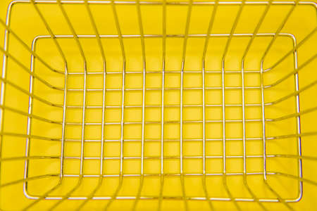 Supermarket grocery basket close-up for shopping.Metal mesh on a yellow background.Space for the text.Background and texture.の写真素材
