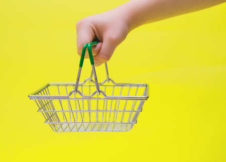 A hand holds a small grocery metal shopping basket in a supermarket.Retail consumer purchases...