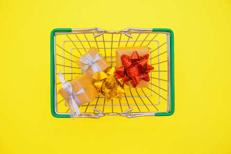 A child's hand holds a small grocery metal shopping basket in a supermarket on a yellow...