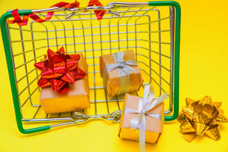 A small metal grocery basket on a yellow background.There are gifts in the basket.Delivery of goods to your home. Space for the text.Buying gifts for the holiday.の写真素材