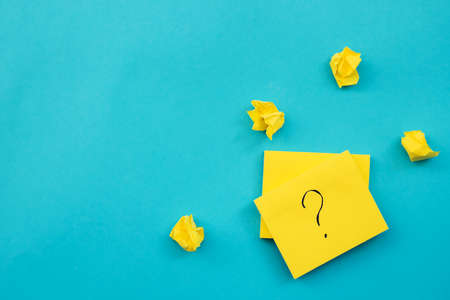 Stickers in the shape of a yellow square are placed on a blue background. Notepads for notes and reminders.There are crumpled wads of paper all around. A question mark is written on the leaf.の写真素材
