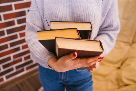 A young woman holds books in her hands. The girl is wearing a sweater and jeans. Student and...
