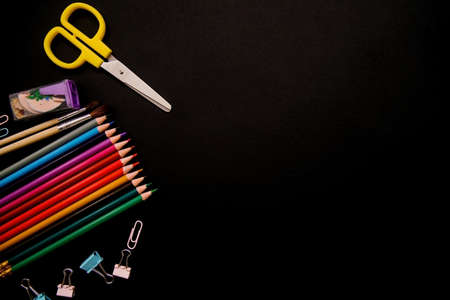 Colored pencils, paper clips, and clips are arranged in a row on a black background. School supplies. Office supplies. Minimalistic style of photography.の写真素材