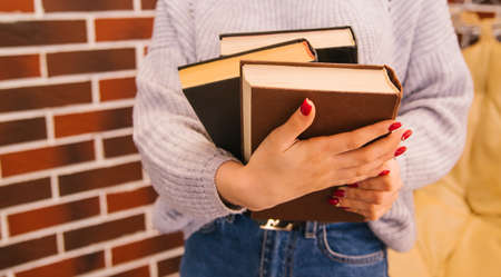 A young woman holds books in her hands. The girl is wearing a sweater and jeans. Student and schoolboy. Books from the library.Textbooks close-up.の写真素材