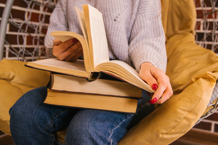 A young woman holds books in her hands. A stack of books sits on her lap. The girl reads and flips through the pages. Student and schoolboy. Books from the library.の写真素材