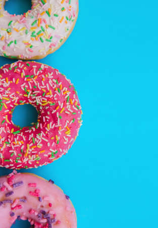 Sweet donuts of different colors are arranged in a row on a blue background. Confectionery products. Harmful fast food.Bright colored background.の写真素材
