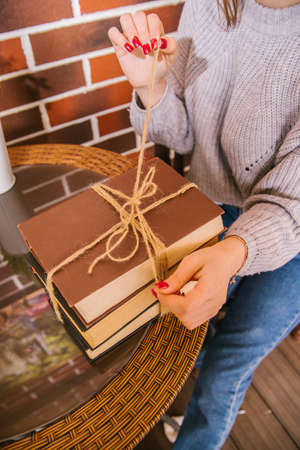 There's a stack of books on the table. The books are tied with string. A young woman is sitting at a...